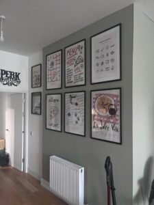 Gallery wall of assorted artwork arranged in a grid pattern in a hallway.